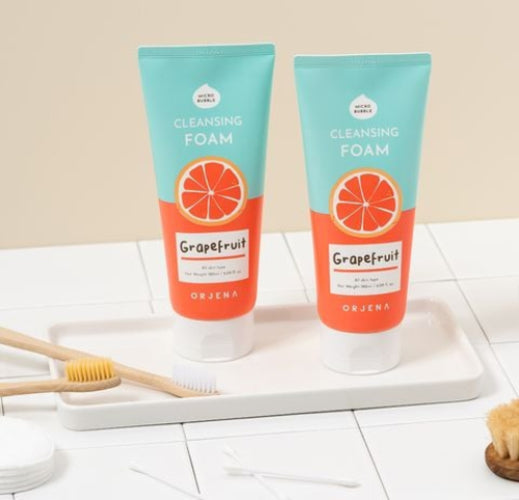 Two tubes of ORJENA Grapefruit Cleansing Foam sit on a white tray alongside wooden toothbrushes and cotton swabs.