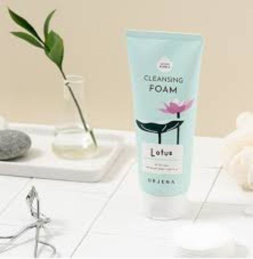 An ORJENA Lotus Cleansing Foam tube displayed on a white tiled surface next to a small glass vase.