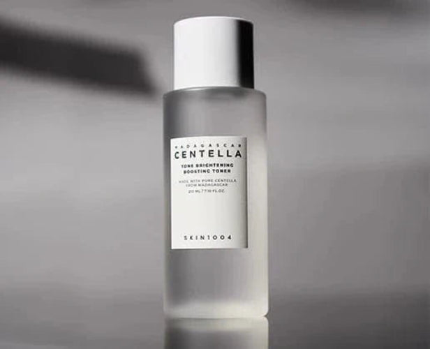 SKIN1004 Madagascar Centella Tone Brightening Boosting Toner frosted glass bottle with white lid against shadowed gray backdrop.
